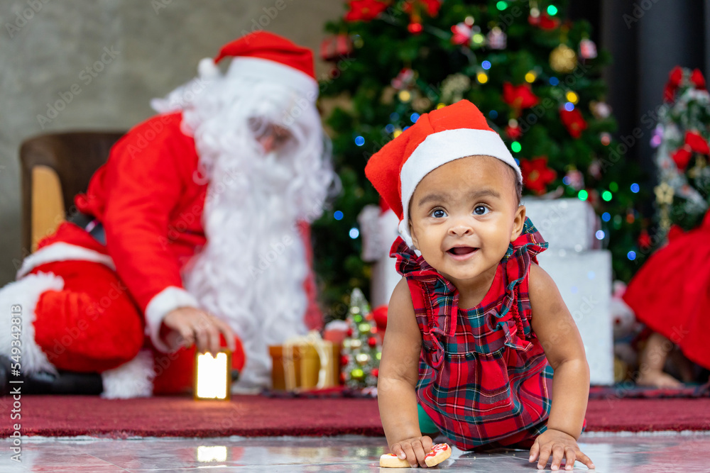 African American baby is having fun playing with toys while Santa claus is preparing gift and sitting behind by the christmas tree for season celebration concept African American baby is having fun playing with toys while Santa claus is preparing gift and sitting behind by the christmas tree for season celebration concept