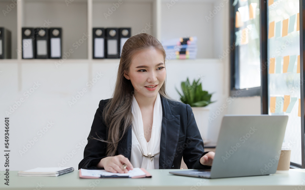 Young attractive Asian business woman with messy desk in office, sitting at the desk, working at contemporary office and documents. working with laptop Young attractive Asian business woman with messy desk in office, sitting at the desk, working at contemporary office and documents. working with laptop