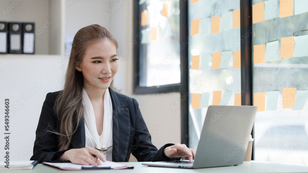 Young attractive Asian business woman with messy desk in office, sitting at the desk, working at contemporary office and documents. working with laptop Young attractive Asian business woman with messy desk in office, sitting at the desk, working at contemporary office and documents. working with laptop