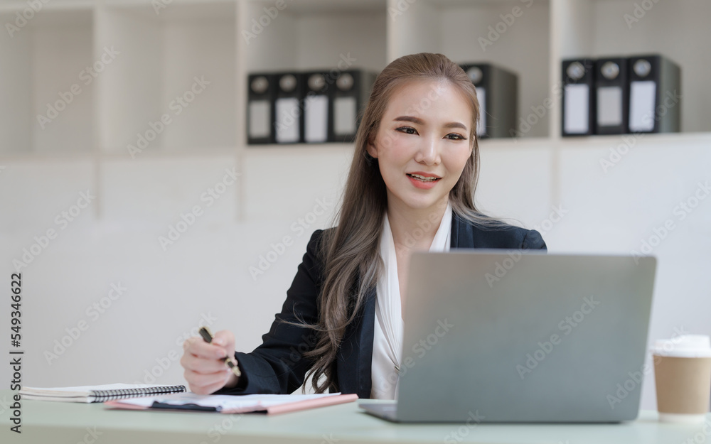 Young attractive Asian business woman with messy desk in office, sitting at the desk, working at contemporary office and documents. working with laptop Young attractive Asian business woman with messy desk in office, sitting at the desk, working at contemporary office and documents. working with laptop