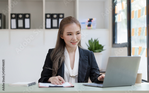 Young attractive Asian business woman with messy desk in office, sitting at the desk, working at contemporary office and documents. working with laptop