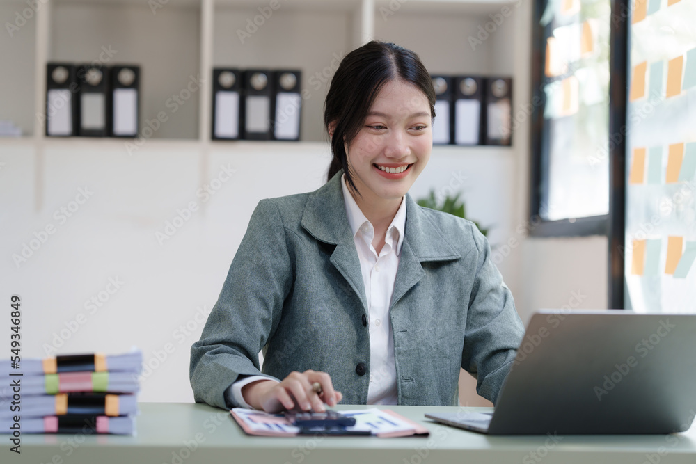 Pretty Asian business woman in black suit working at her office desk, with document file and paperwork. working with laptop Pretty Asian business woman in black suit working at her office desk, with document file and paperwork. working with laptop