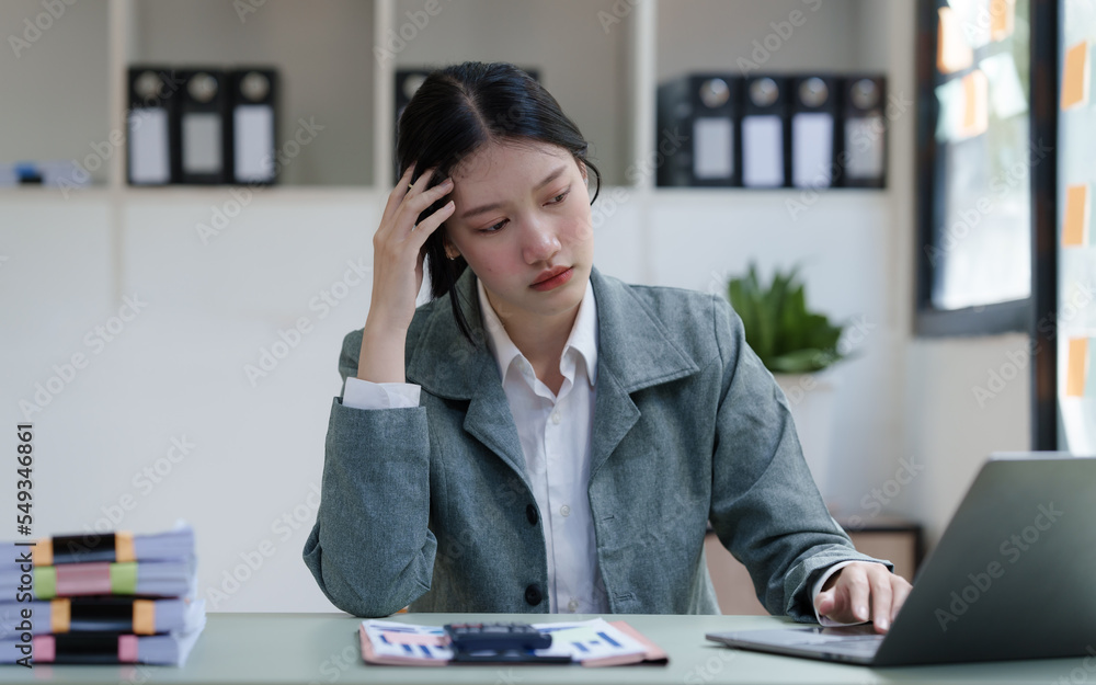 Pretty Asian business woman in black suit working at her office desk, with document file and paperwork. feeling stressed, headache Pretty Asian business woman in black suit working at her office desk, with document file and paperwork. feeling stressed, headache