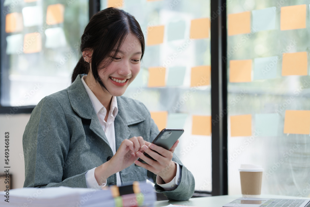 Pretty Asian business woman in black suit working at her office desk, with document file and paperwork. texting mobile smartphone or chat message Pretty Asian business woman in black suit working at her office desk, with document file and paperwork. texting mobile smartphone or chat message