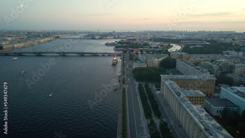 Aerial parallel view of the warship Aurora next to bridge in historical and at the same time modern city of  St. Petersburg on a summer evening