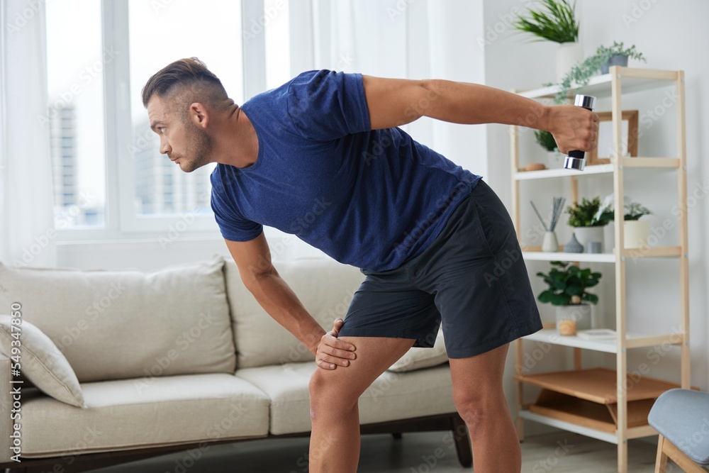 Man sportsman training at home with dumbbells, exercises for arms and back muscles, strong body and correct posture, the concept of health and beauty Man sportsman training at home with dumbbells, exercises for arms and back muscles, strong body and correct posture, the concept of health and beauty