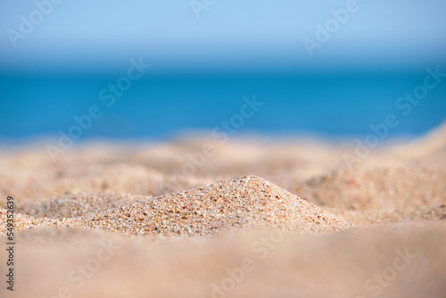 Close up of clean yellow sand surface covering seaside beach with blue sea water on background. Travel and vacations concept