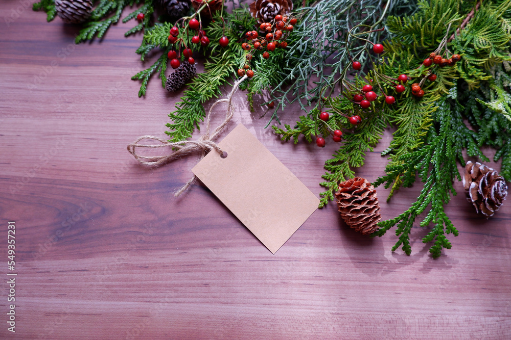 Fototapeta premium Christmas and winter holiday decoration background composition with winter green, acorns, winter berries and blank tag. Christmas holiday botanical background for banner, background and design.