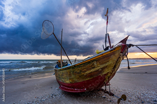 A wooden fishing boat on a beach with a stormy shy overhead at Mui Ne in Vietnam