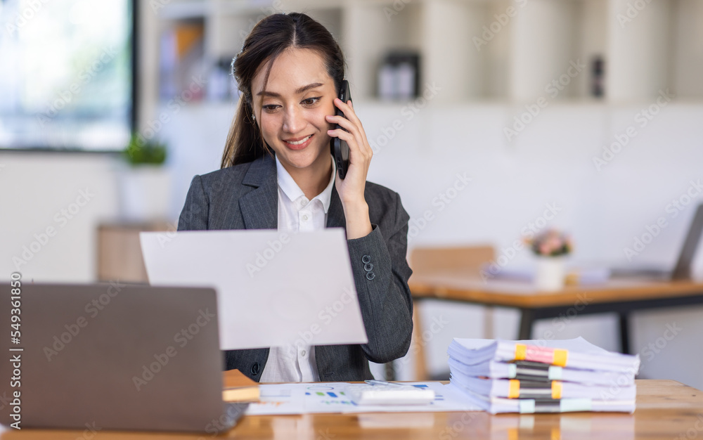 Asian female business analyst financial advisor call phone and preparing statistic report studying documents on work desk, Asian business woman work with documents in the office. Asian female business analyst financial advisor call phone and preparing statistic report studying documents on work desk, Asian business woman work with documents in the office.