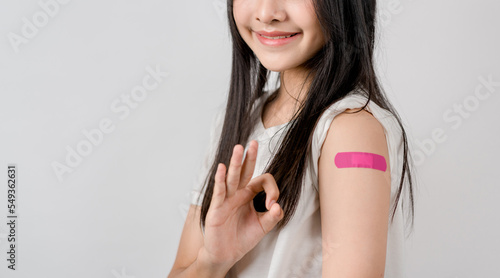 Happy young woman show ok sign after getting a vaccine. showing shoulder with bandage after receiving vaccination, herd immunity, side effect, booster dose, vaccine passport and Coronavirus pandemic