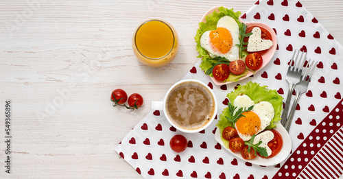 Festive breakfast on Valentine's Day. Banner Two heart-shaped plates with fried eggs, tomatoes and cheese, coffee and juice on a white wooden table. View from above. Banner. Healthy breakfast.