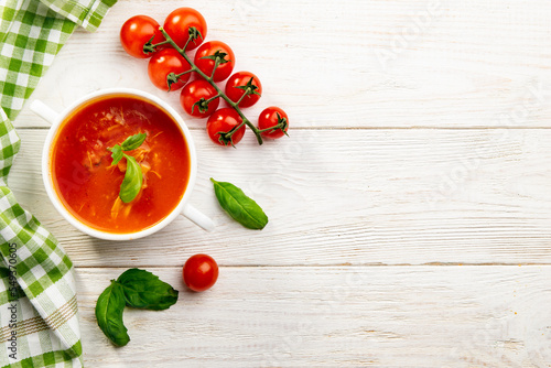 Red tomato soup with basil on white wooden table