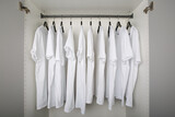 white t-shirts hang on a clothes rail in a white wardrobe. all t-shirts are the same color and size and are worn on hangers