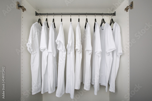 white t-shirts hang on a clothes rail in a white wardrobe. all t-shirts are the same color and size and are worn on hangers photo