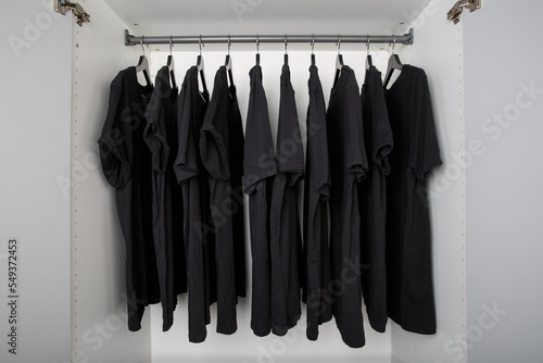 black t-shirts hang on a clothes rail in a white wardrobe. all t-shirts are the same color and size and are worn on hangers photo