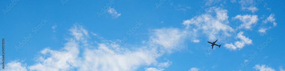 The passenger airplane is flying far away in the blue sky and white clouds. Plane in the air. International passenger air transportation. Banner or header - obrazy, fototapety, plakaty 