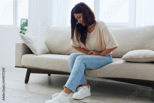 Woman sitting on sofa at home back and stomach pain during menstruation, women's day, women's health problems, suspected appendicitis