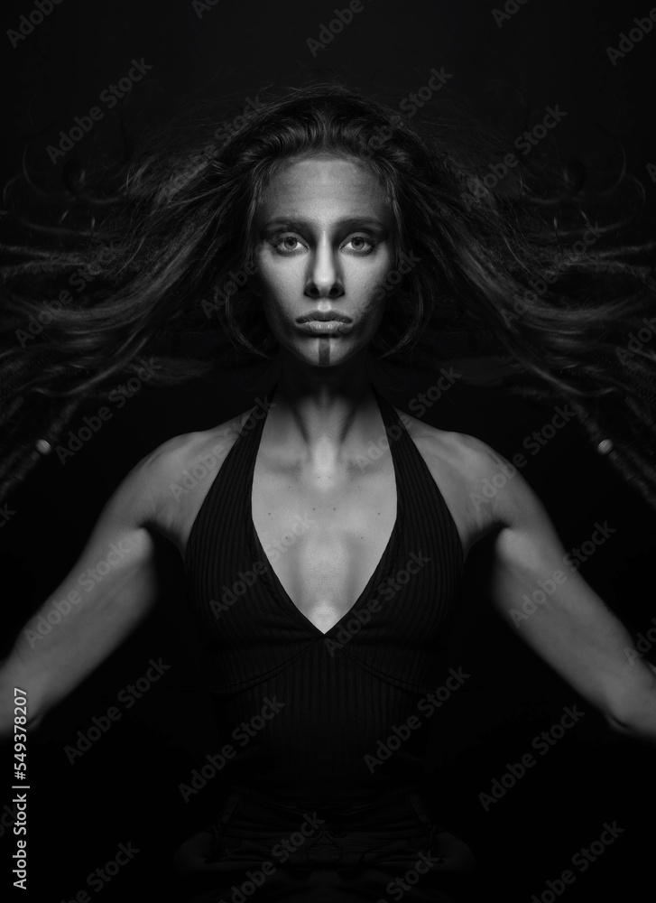 Fine art and sci-fi concept. Abstract and futuristic looking alien or extraterrestrial close-up portrait. Model hair floating in air with raised arms looking at camera. Black and white image