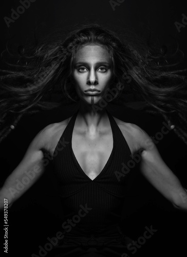 Fine art and sci-fi concept. Abstract and futuristic looking alien or extraterrestrial close-up portrait. Model hair floating in air with raised arms looking at camera. Black and white image