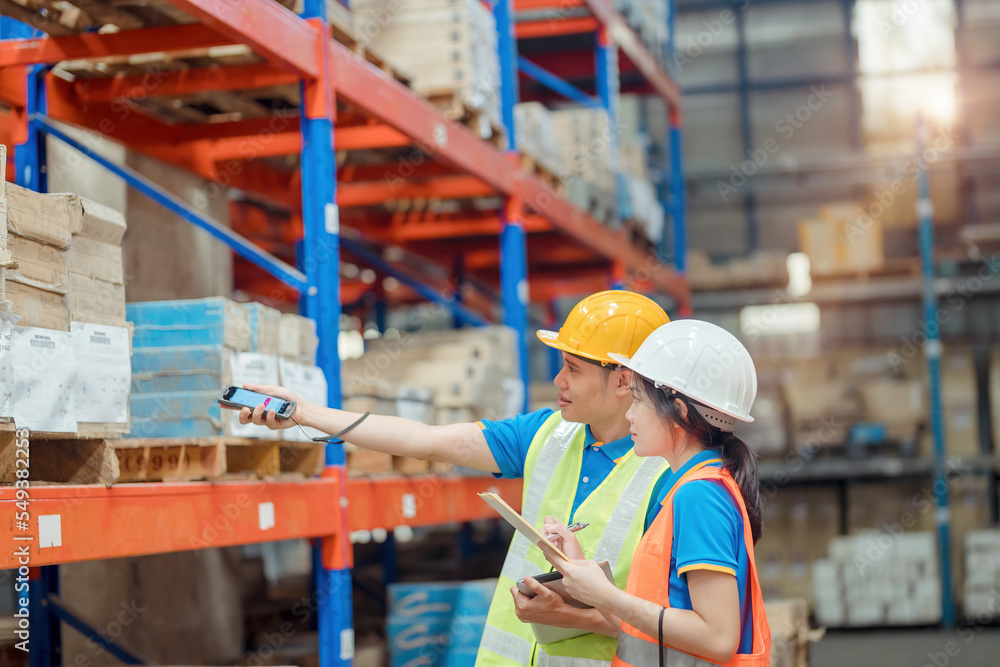 Asian engineer in helmets order and checking goods and supplies on shelves with goods background in warehouse.logistic and business export ,Warehouse worker checking packages on shelf in a large store Asian engineer in helmets order and checking goods and supplies on shelves with goods background in warehouse.logistic and business export ,Warehouse worker checking packages on shelf in a large store