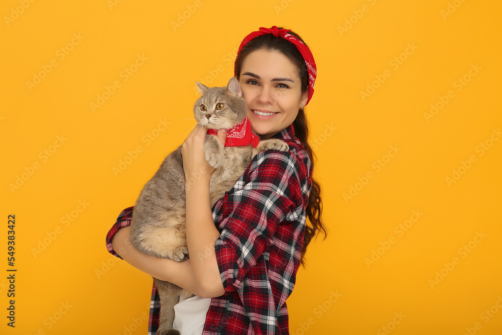 Young woman with adorable cat on yellow background, space for text