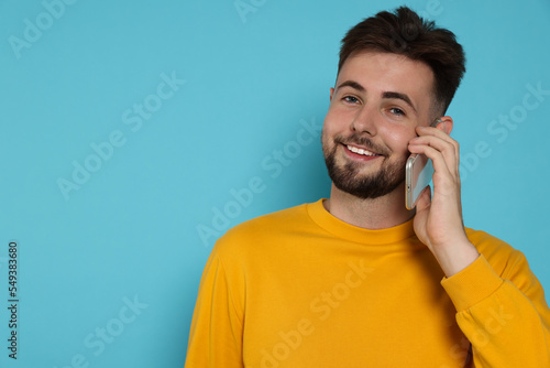 Handsome man in yellow sweatshirt talking on phone against light blue background, space for text