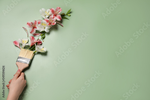 Woman holding painting brush and beautiful alstroemerias on green background, closeup. Space for text photo