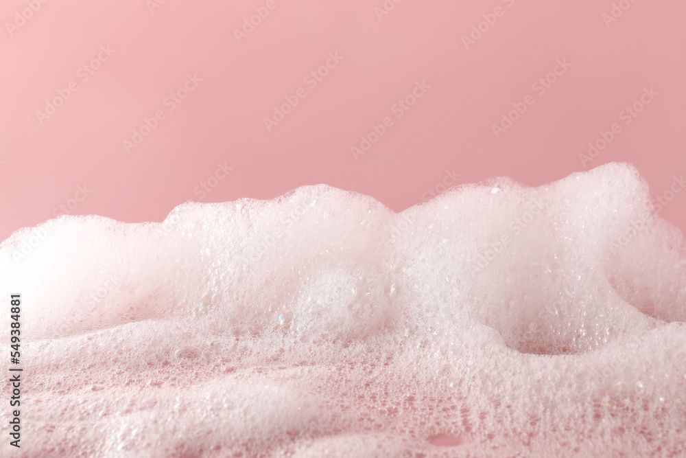 Fluffy bath foam on pink background, closeup. Care product