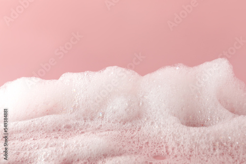 Fluffy bath foam on pink background, closeup. Care product