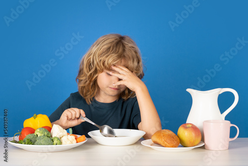 Bad appetite. Sad kid eating healthy food on studio iosolated background. Baby eat soup with spoon. Kid eating soup. photo