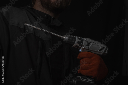 Hand holds cordless electric screwdriver with bit for screws and drilling isolated on black background