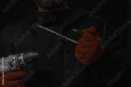 Hand holds cordless electric screwdriver with bit for screws and drilling isolated on black background