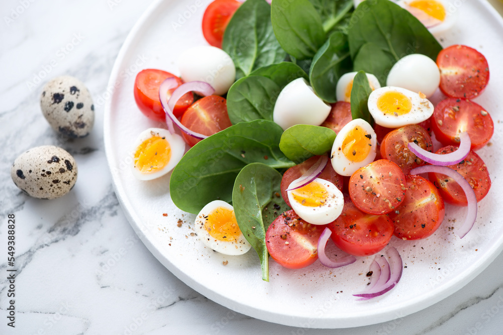 Close-up of salad with spinach leaves, red cherry tomatoes, quail eggs and red onion served on a white plate, selective focus Close-up of salad with spinach leaves, red cherry tomatoes, quail eggs and red onion served on a white plate, selective focus