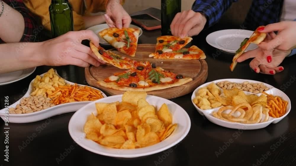 Close-up of a group of friends simultaneously taking slices of sliced pizza in a cafe, friends relax in a restaurant and eat pizza. Close-up of freshly baked pizza on the table in a cafe. Close-up of a group of friends simultaneously taking slices of sliced pizza in a cafe, friends relax in a restaurant and eat pizza. Close-up of freshly baked pizza on the table in a cafe.