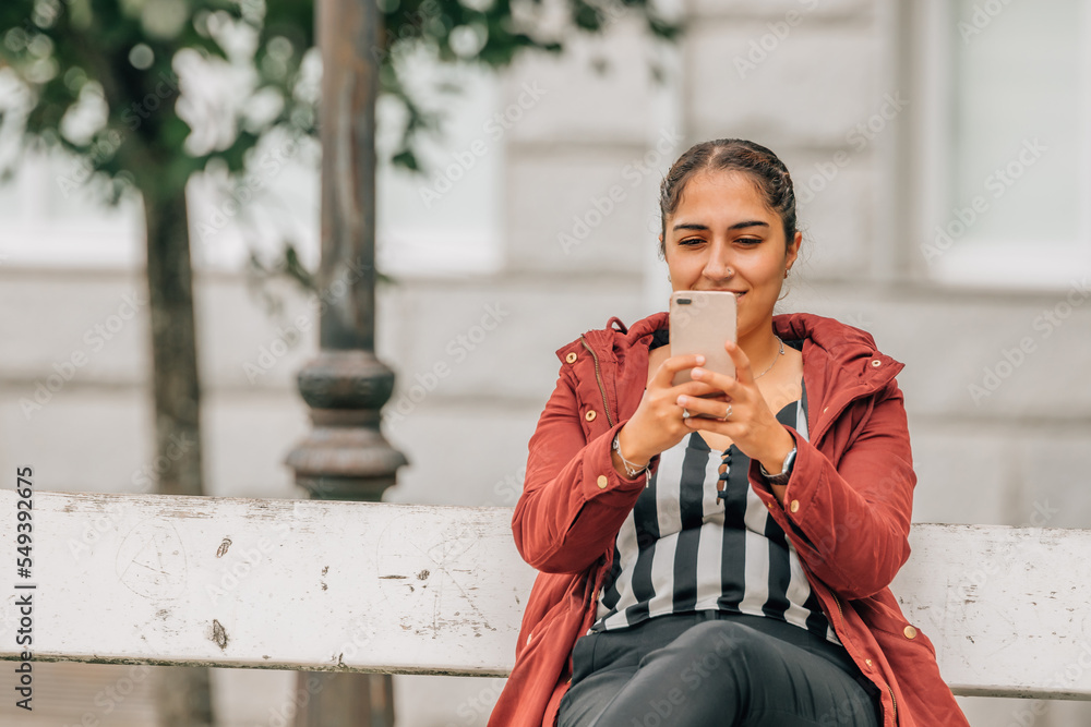 Fototapeta premium young woman on park bench with mobile phone