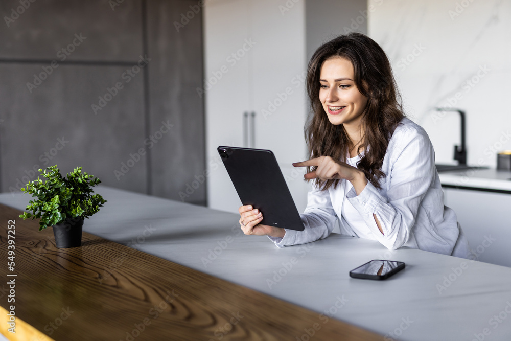 Happy woman using digital tablet sitting in kitchen at home. Happy woman using digital tablet sitting in kitchen at home.