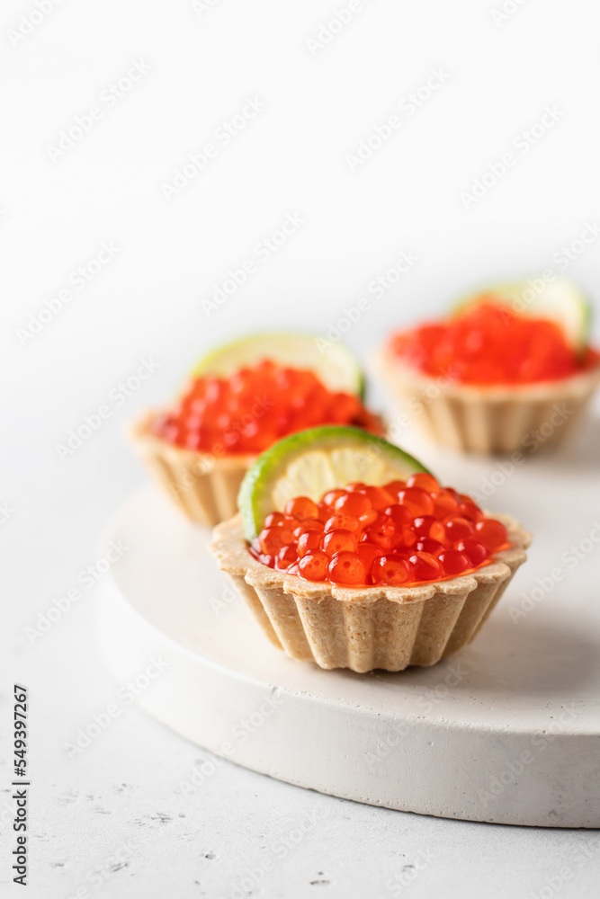Festive New Year appetizer tartlets stuffed with red caviar and a slice of lime close up on a white tray with copy space. Christmas or new year food recipe Festive New Year appetizer tartlets stuffed with red caviar and a slice of lime close up on a white tray with copy space. Christmas or new year food recipe