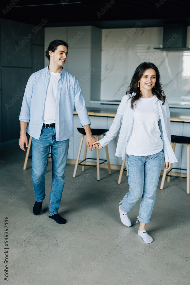 Fototapeta premium Attractive young woman and handsome man are enjoying spending time together while standing on light modern kitchen with cup of coffee in hands.