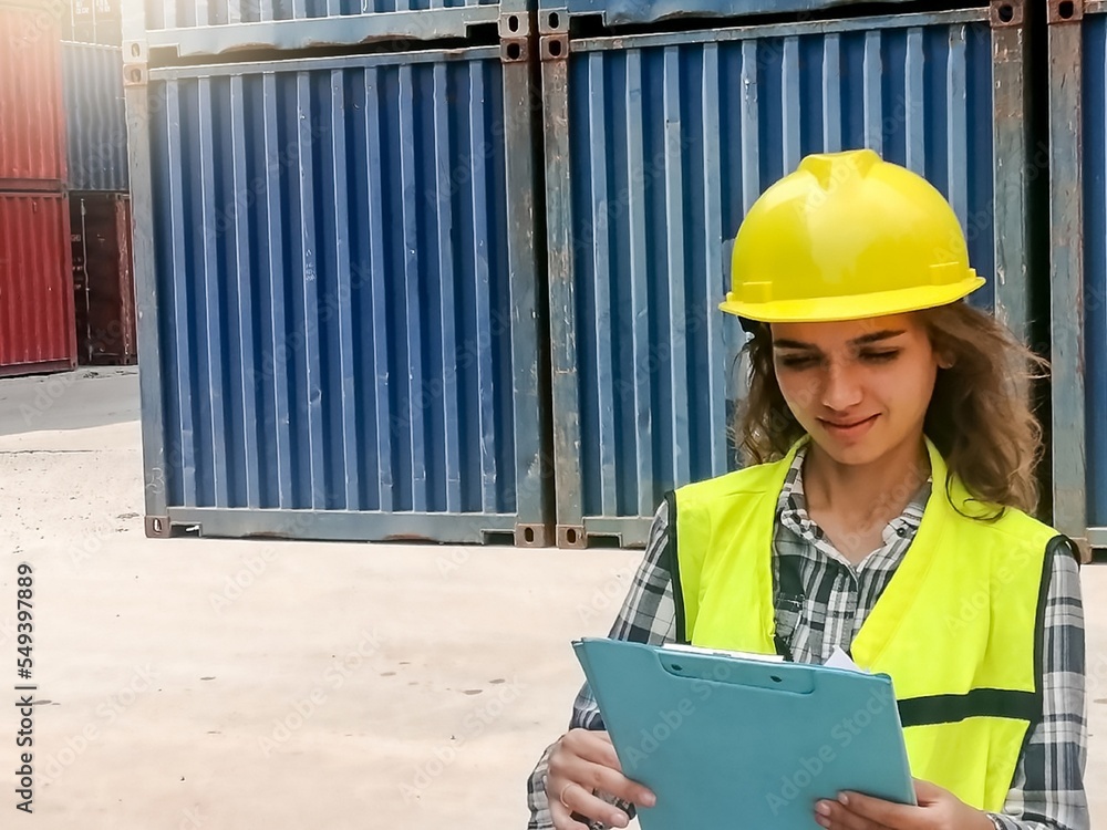 A female worker in helmets and uniforms review reports at a freight container shipping company. A female worker in helmets and uniforms review reports at a freight container shipping company.