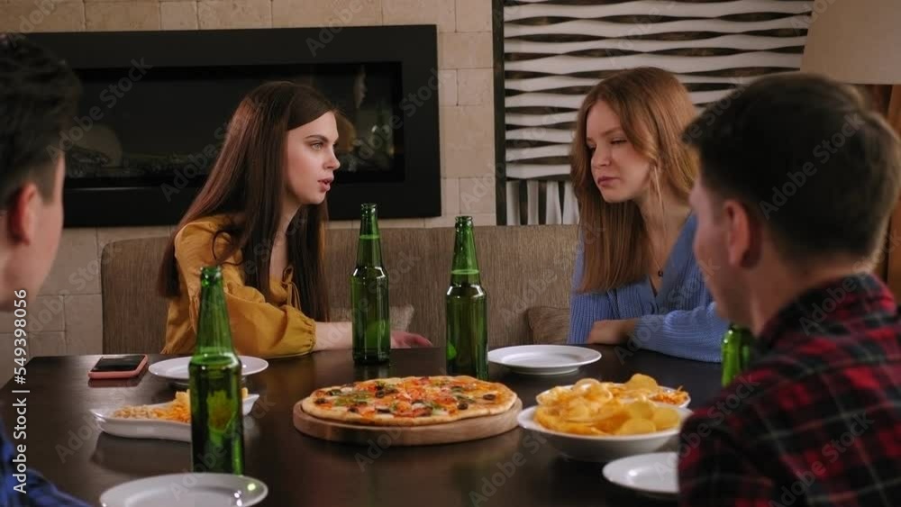 Close-up of two girls in a bar sitting at a table with two guys drinking beer and eating pizza, students relaxing at the bar. Close-up of two girls in a bar sitting at a table with two guys drinking beer and eating pizza, students relaxing at the bar.
