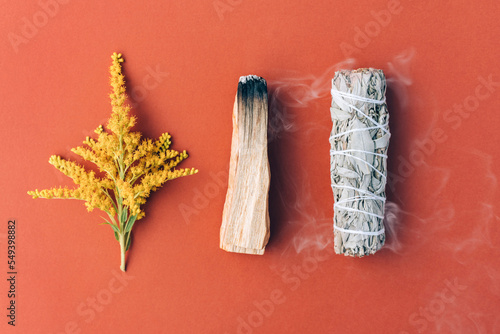 Burning incenseю White sage and palo santo stick with smoke over red brown background. Bundle for meditation and room fumigation. Selective focus. Flat lay style