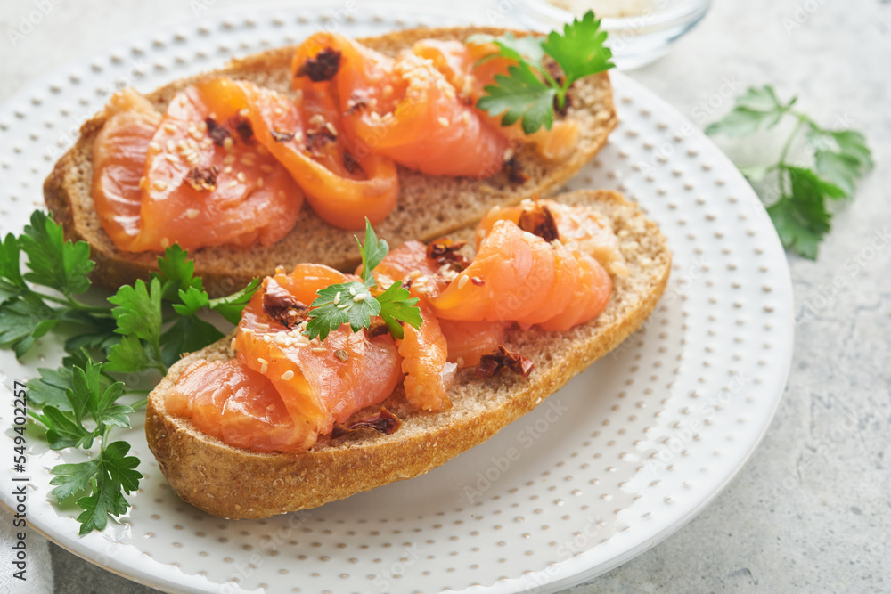 Sandwiches with salted salmon. Open sandwiches from cereal or whole grain rye bread with salted salmon, sesame seeds and dried tomato on white marble stand. Seafood. Healthy food. Scandinavian cuisine