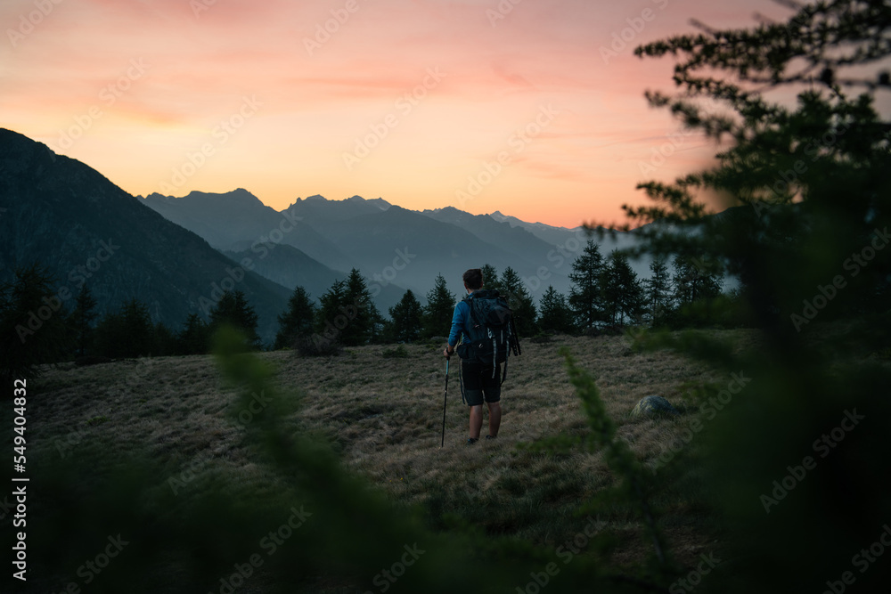 A hiker is exploring the area of Mount Berlinghera after sunset, with a colorful sky in the background