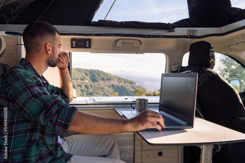 Fotografia, Obraz young man working on his laptop from his camper van in the middle of the nature,