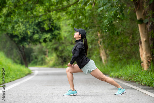 Healthy woman warming down stretching her legs and looking away in the road outdoor. Asian runner woman workout before fitness and jogging session at the park. Health care Lifestyle Concept.