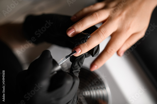 Manicurist hands in gloves covering the nail with transparent base under shellac