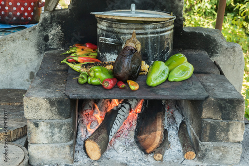 Roasting peppers and eggplant on iron plate on outdoor rustic hearth