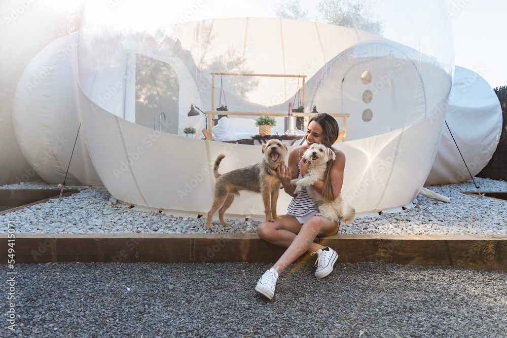 Cheerful woman petting dogs outside glamping tent - obrazy, fototapety, plakaty 