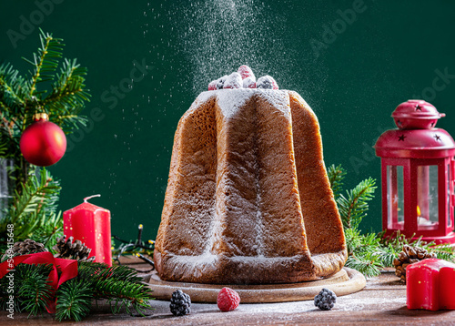 Traditional Italian Christmas cake Pandoro on wooden table with Christmas decoration, lights on green background, icing sugar is powdering to top photo